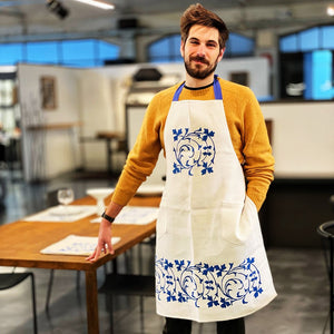 a man wearing a white linen apron with hand printed blue decorations